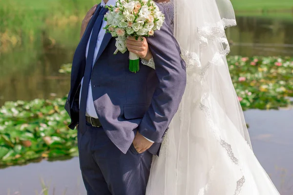 Bride with bouquet in hand hugging groom — Stock Photo, Image