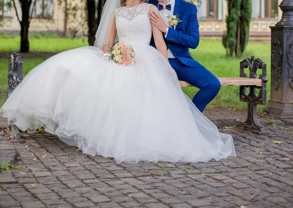 A noiva e o noivo sentam-se juntos no banco — Fotografia de Stock