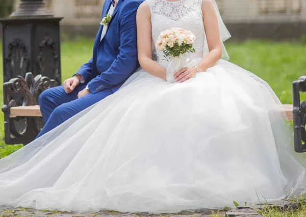 A noiva e o noivo sentam-se em um banco no parque — Fotografia de Stock