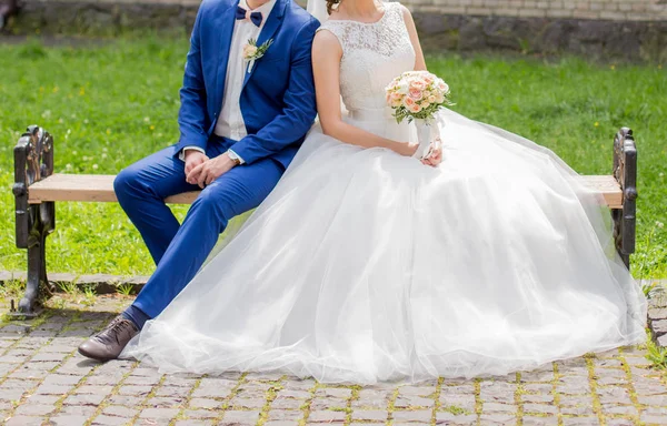 Bruden och brudgummen sitter på en bänk i parken — Stockfoto