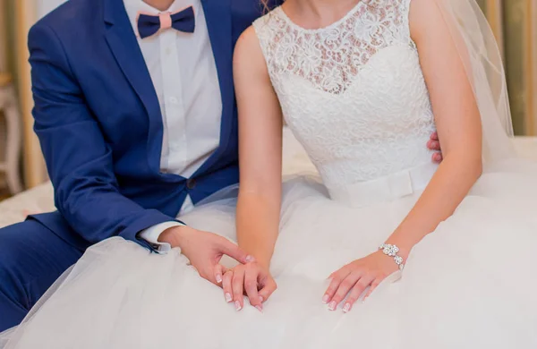 Bruden och brudgummen sitter på sängen och hålla händerna — Stockfoto