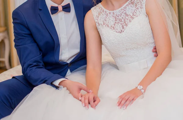 Bruden och brudgummen sitter på sängen och hålla händerna — Stockfoto