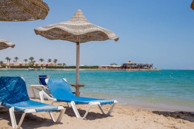 kum plajındaki hasır şemsiyeler altında mavi şezlong