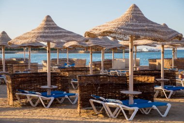 şezlong ve güneş ışıklı plajda hasır şemsiyeler