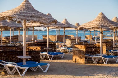 şezlong ve güneş ışıklı plajda hasır şemsiyeler