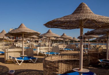 şezlong ve güneş ışıklı plajda hasır şemsiyeler