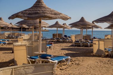 şezlong ve güneş ışıklı plajda hasır şemsiyeler