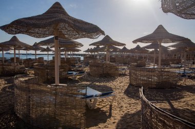 şezlong ve güneş ışıklı plajda hasır şemsiyeler
