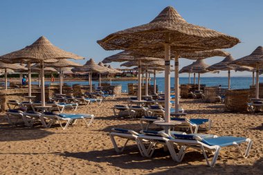 şezlong ve güneş ışıklı plajda hasır şemsiyeler