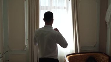 Takım elbiseli bir adam pencerenin yanında duruyor.