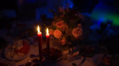 Masanın üzerindeki karanlıkta kırmızı mumlar yanıyor.