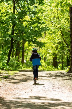 Çocuk parkta kasklı bir scooterla yalnız.