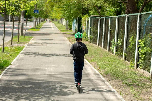 child alone in the park on scooter in a helmet