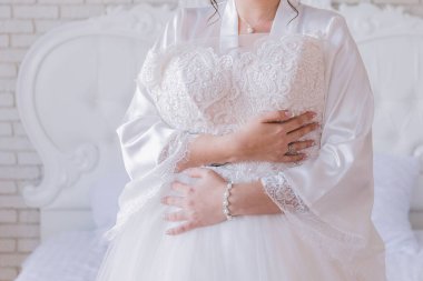 Peignoir giymiş gelin gelinliğini tutuyor.