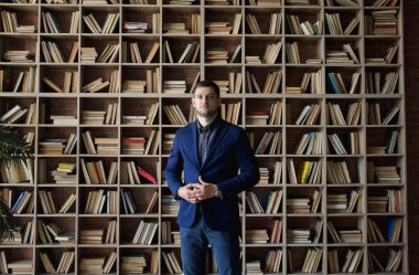 Kütüphanede elinde kitapla ceketli bir adam.