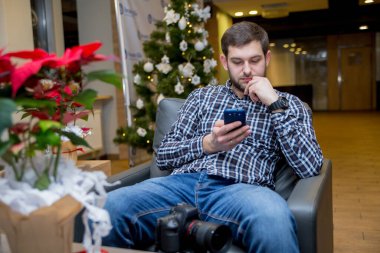 Bir adam elinde telefonla sandalyede oturuyor.