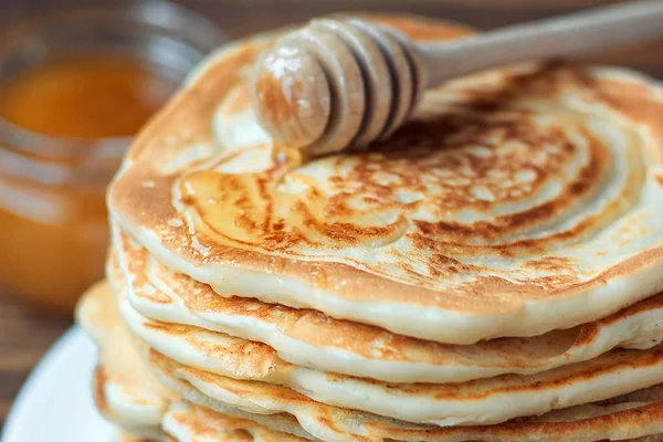 Stack of delicious, homemade pancakes with honey on white plate on wooden background. Healthy breakfast, close up. Pancake's Day. High stack of pancakes shallow DOF. — Stock Photo, Image