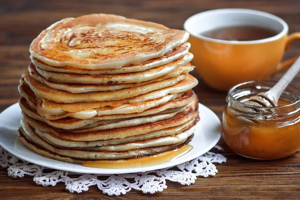 Στοίβα από λαχταριστά, σπιτικά τηγανίτες με μέλι σε λευκή πινακίδα σε ξύλινο υπόβαθρο. Υγιεινό πρωινό, κοντινό πλάνο. Ημέρα της τηγανίτα. Υψηλή στοίβα τηγανίτες ρηχά Dof. — Φωτογραφία Αρχείου