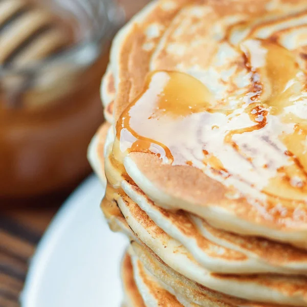 Stack of delicious, homemade pancakes with honey on white plate on wooden background. Healthy breakfast, close up. Pancake's Day. High stack of pancakes shallow DOF. — Stock Photo, Image