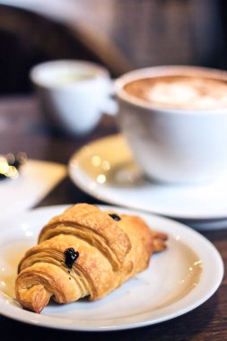 Lezzetli kruvasan ve kahve. Kahve fincanı ve ahşap zemin üzerine taze pişmiş kruvasanlar ile kahvaltı. Vintage etkisi tarzı resimler. Seçici odak. Sığ derinlik-in tarla.