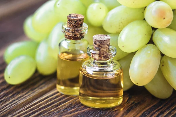 Curando óleo de sementes de uvas em um frasco de vidro, uvas frescas no fundo de madeira velha, extrato de semente tem antioxidante e nutrir a pele, conceito de spa, foco seletivo macro vista frontal. Biologia, produtos ecológicos . — Fotografia de Stock