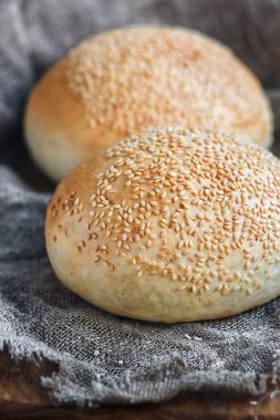 Yuvarlak topuz, susam çörek, ekmek rulo. Ahşap, çuval bezi zemin üzerine susam ile lezzetli hamburger ekmeği. Taze pişmiş hamburger ekmeği. Üstten Görünüm.