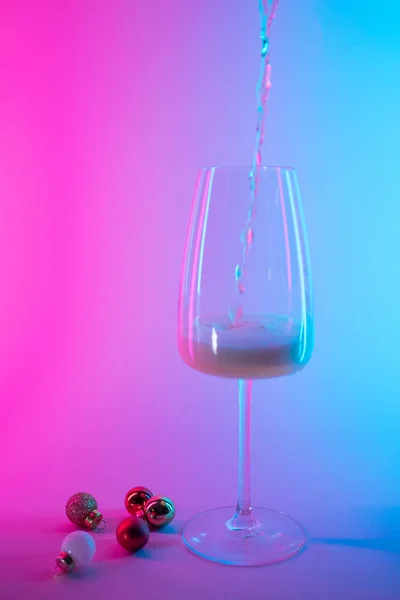 ピンクと青のネオングラデーションの光でクリスマスツリーボールの装飾を持つワインの空のガラス — ストック写真
