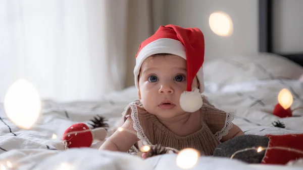 Kırmızı Noel Baba şapkalı, ışıklı küçük tatlı kız portresi.