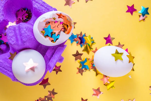 Eieren met stervormige confetti in paars karton op gele achtergrond. Feestelijke versieringen — Stockfoto