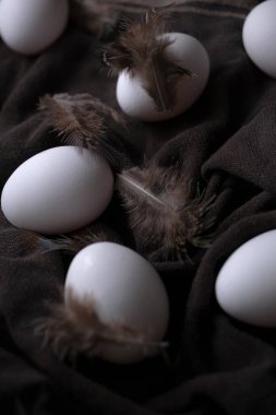 Karanlık ruh hali konseptinde paskalya yumurtaları siyah tekstil arka planında kuş tüyü ile ışık