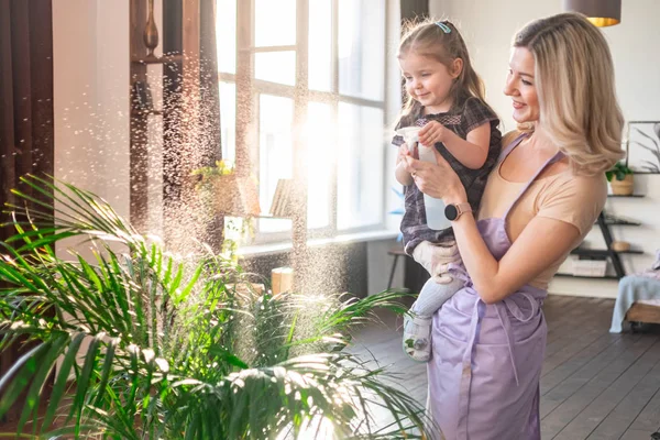 Jeune femme attrayante avec son tout-petit fille arrosant des plantes à la maison. Faire du travail domestique — Photo