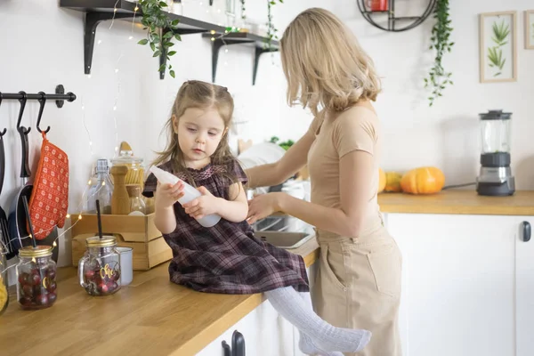 Jonge moeder maakt huishoudelijk werk in de keuken met haar peuterdochter. Huishoudelijk leven — Stockfoto