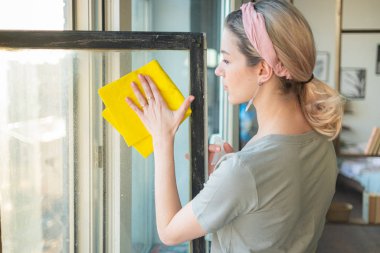 Eldivenli bir kadın, evinde bez ve temizleyici sprey ile pencereyi temizliyor. ev işi ve ev idaresi kavramı