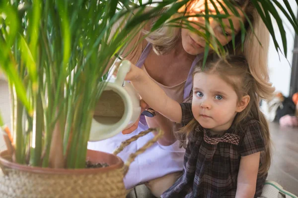 Jeune femme attrayante avec son tout-petit fille arrosant des plantes à la maison. Faire du travail domestique — Photo