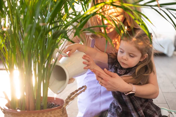 Jeune femme attrayante avec son tout-petit fille arrosant des plantes à la maison. Faire du travail domestique — Photo