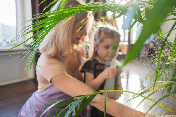 Jonge aantrekkelijke vrouw met haar peuter meisje water geven planten in huis. Huishoudelijk werk — Stockfoto