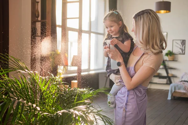 Jeune femme attrayante avec son tout-petit fille arrosant des plantes à la maison. Faire du travail domestique — Photo
