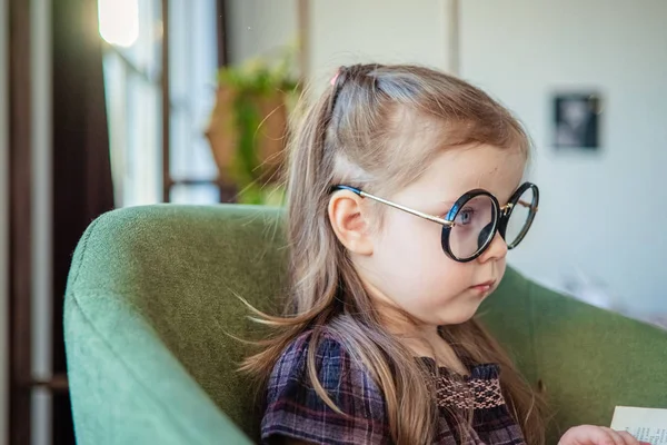 Een klein peutermeisje met een bril die een boek leest. terug naar school concept — Stockfoto