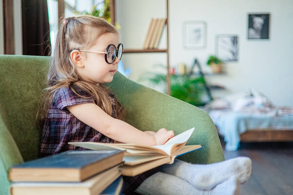 little toddler girl in glasses reading a book. back to school concept