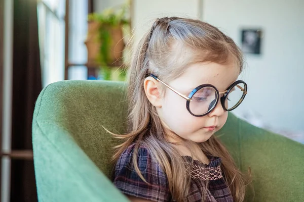 Een klein peutermeisje met een bril die een boek leest. terug naar school concept — Stockfoto