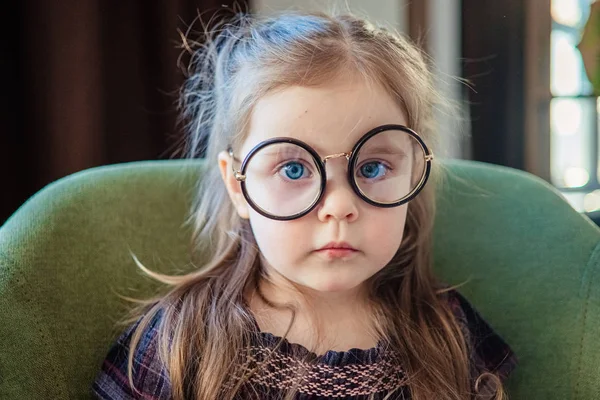 Een klein peutermeisje met een bril die een boek leest. terug naar school concept — Stockfoto