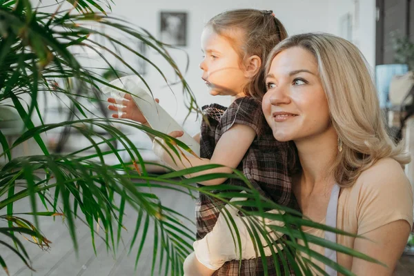 Młoda atrakcyjna kobieta z małą dziewczynką podlewającą rośliny w domu. Wykonywanie prac domowych — Zdjęcie stockowe