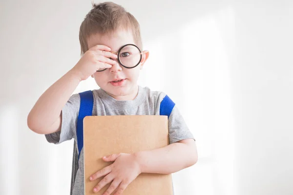 Sırt çantası ve kitabı olan gözlüklü küçük çocuk. Gözlüklü anaokulu öğrencisi. Okul konseptine dönelim. — Stok fotoğraf