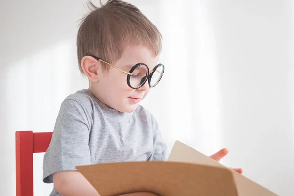 可爱的蹒跚学步的男孩戴着眼镜看书。聪明的学龄前儿童。回到学校的概念 — 图库照片