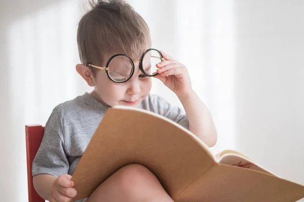 Leuke peuter die een boek leest in een bril. Slimme kleuter. Terug naar schoolconcept — Stockfoto