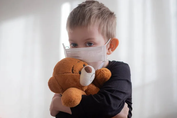 Menino de máscara médica abraçando seu ursinho de pelúcia. Início isolamento coronavírus covid-2019 quarentena — Fotografia de Stock
