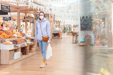 Woman in medical face mask walking in modern grocery market, shop. Corona virus protection, quarantine, self distancing clipart