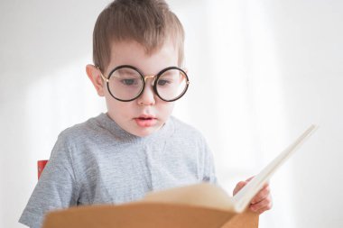 Gözlükle kitap okuyan tatlı çocuk. Zeki anaokulu öğrencisi. Okul konseptine dönelim.