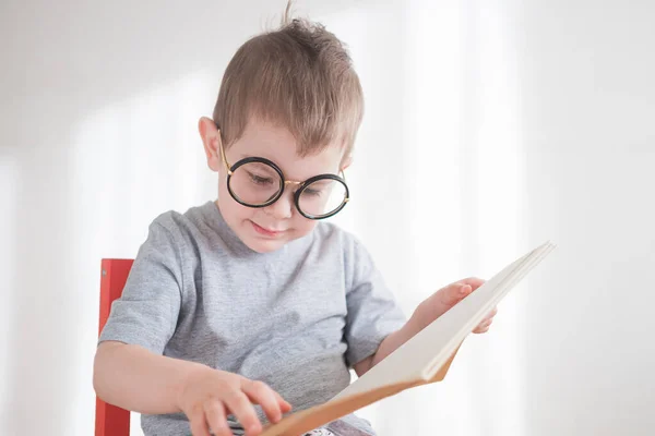 Leuke peuter die een boek leest in een bril. Slimme kleuter. Terug naar schoolconcept — Stockfoto