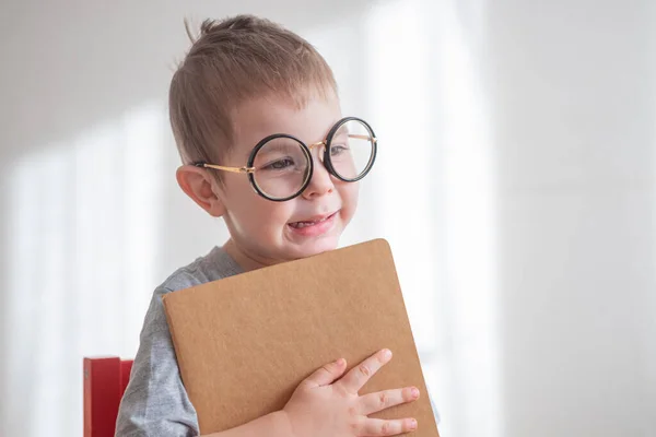 Petit garçon d'âge préscolaire mignon tout-petit dans des lunettes avec un livre regardant directement la caméra. Concept de retour à l'école — Photo